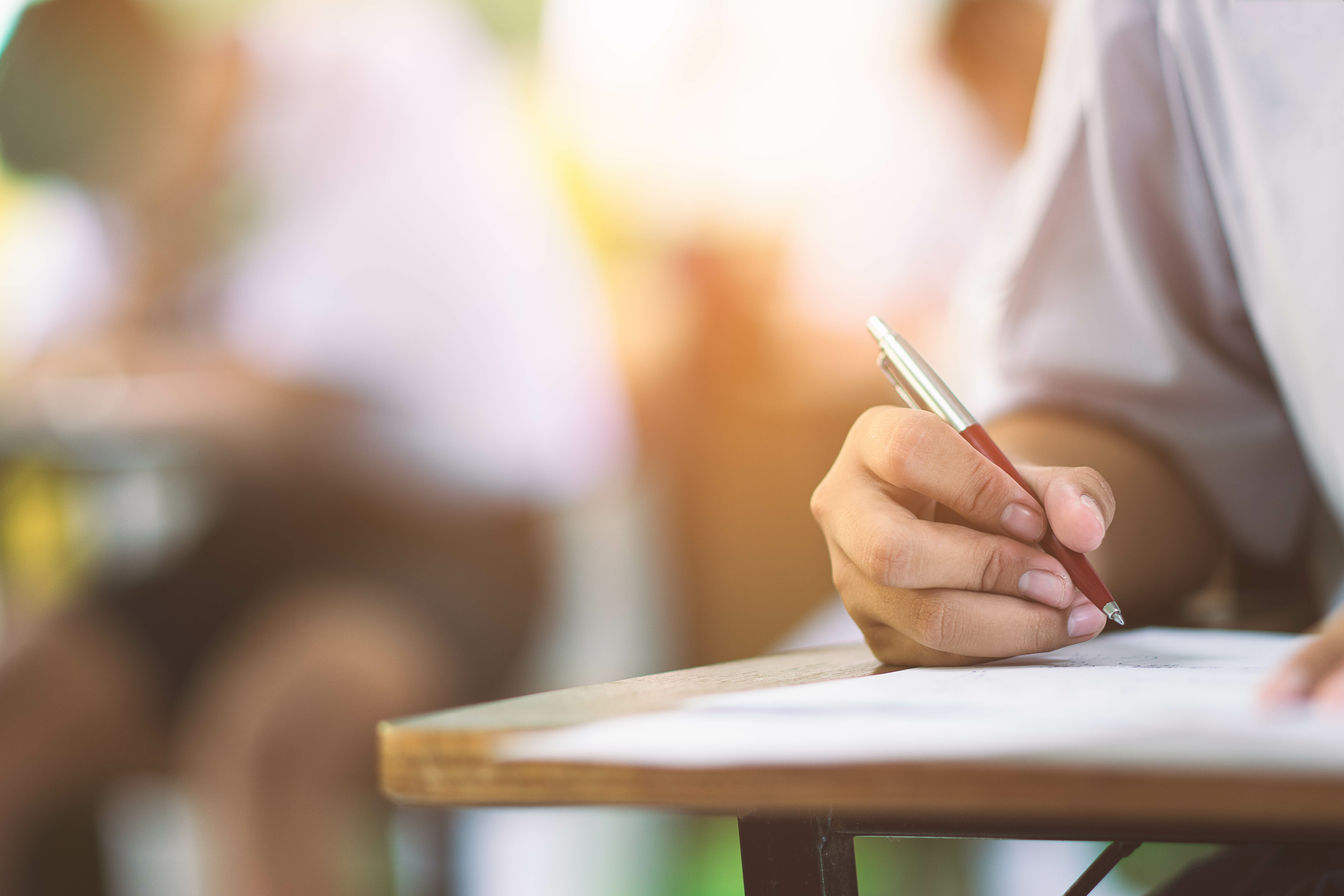 Closeup to hand of student  holding pen and taking exam in classroom with stress for education test .