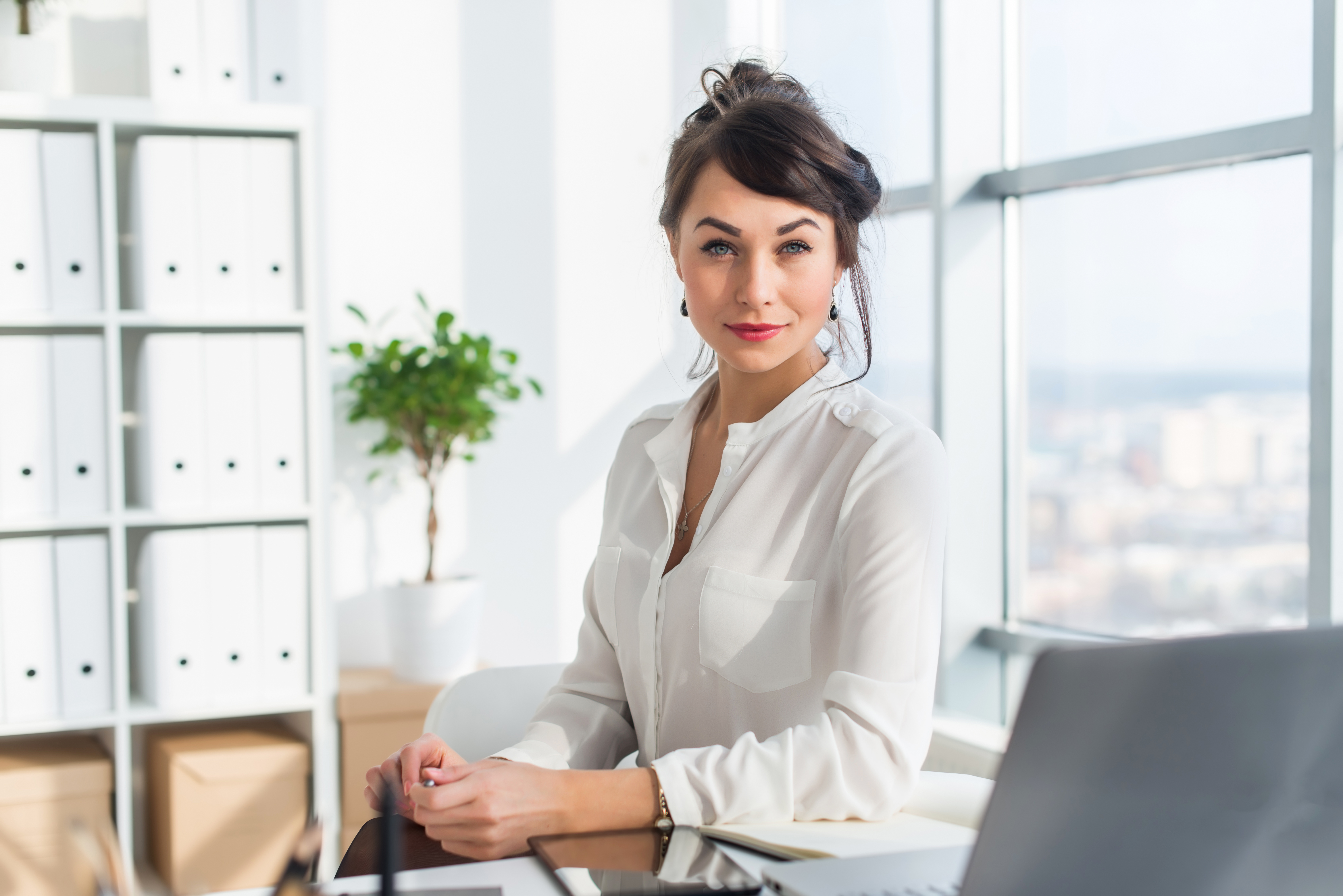 Close-up portrait of a woman sitting in modern loft office, smiling, looking at camera. Young confident female business worker ready for the work day