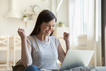 Positive female student in casual wear overjoyed about admission to university after receiving good news by email. Happy young graduate with laptop celebrating getting job after reading notification