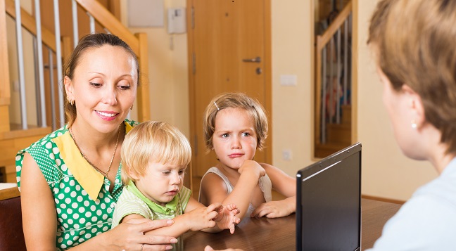 Smiling mother with two little children glad hearing words of social worker at home