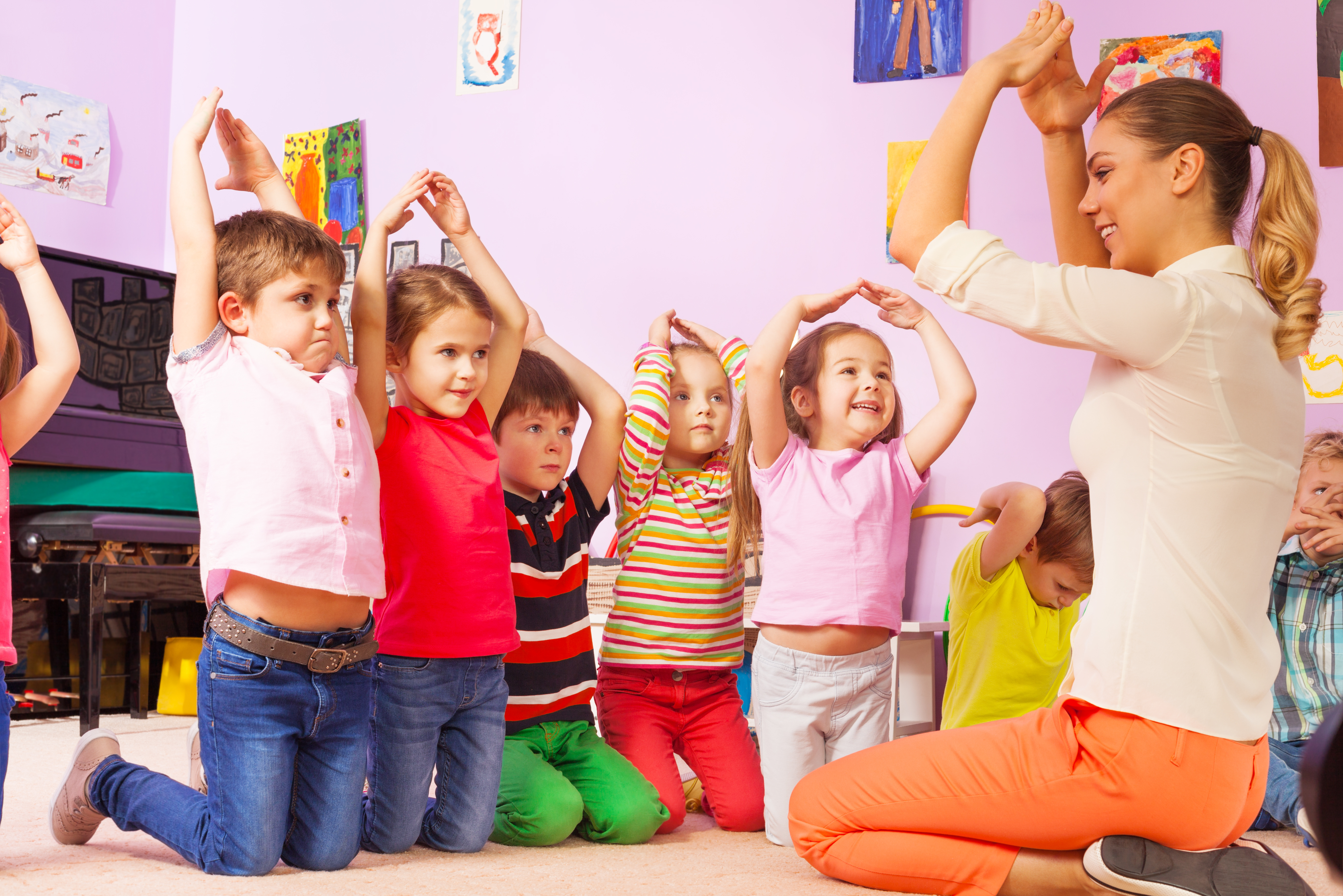 Group of kids repeat gesture after the teacher in kindergarten class making house with hands above head