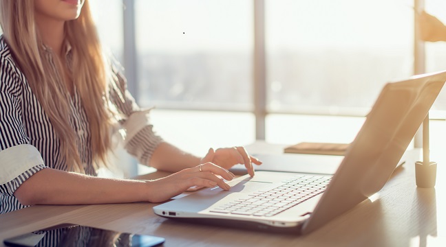 Woman blogging in spacious office using computer on her workplace. Female employee sitting, smiling, looking at camera